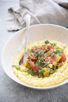 a white bowl filled with grits topped with tomatoes and spinach garnish