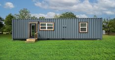 a house made out of shipping containers in the middle of a grassy field with stairs leading up to it