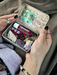 a woman is holding an open tin with various items in it and her hands are on top of the tin