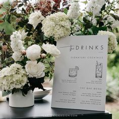 the drinks menu is next to some white flowers in vases on a black table