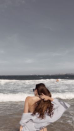 a woman sitting on the beach with her hair blowing in the wind and looking at the ocean