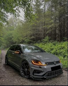 a grey car parked on the side of a dirt road in front of some trees