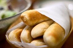 some bread rolls in a basket on a table next to a glass bowl and spoon