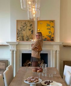 a woman standing in front of a table with donuts and drinks on it, next to a fireplace