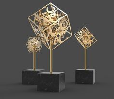 three golden sculptures on black pedestals with one sculpture in the shape of a cube