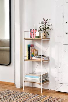 a white shelf with books and plants on it in front of a wall mounted mirror