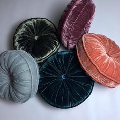 four velvet round cushions in various colors on a white surface with one cushion folded up to the side