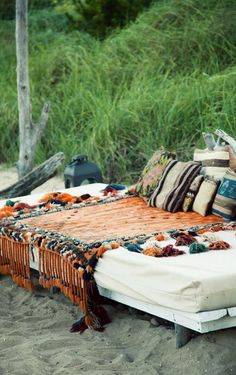 an image of a bed with blankets and pillows on it in front of some tall grass