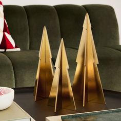 three gold christmas trees sitting on top of a table next to a green velvet couch