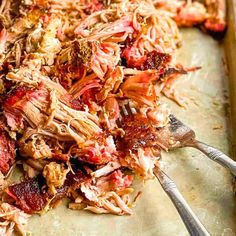 shredded meat sitting on top of a cutting board next to utensils and a fork