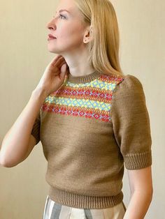 a woman wearing a brown sweater and tan pants with her hand on her chin looking up