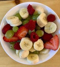 a white bowl filled with fruit on top of a wooden table