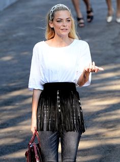 a woman is walking down the street with her hand in her pocket and holding a purse