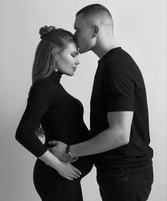 a man and woman standing next to each other in front of a white wall kissing