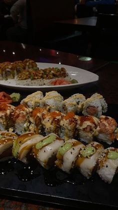 sushi rolls and other food items on a black tray in front of a glass table