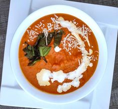 a white plate topped with a bowl of tomato soup and garnished with parmesan cheese