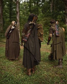 three people dressed in medieval clothing walking through the woods with bows and arrows on their heads