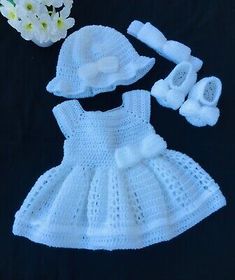 a crocheted baby dress and booties with flowers on the table next to it