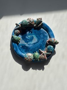 a blue bowl with sea shells and starfish on the bottom is sitting on a white surface