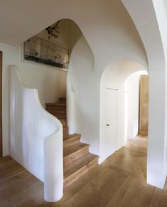 an arched doorway leads to a white staircase with wood floors and wooden steps leading up to the second floor