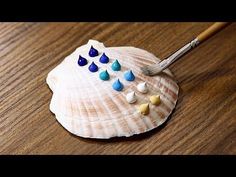 a small seashell with blue, white and yellow drops on it next to a paintbrush