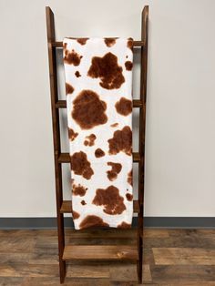 a brown and white cow print blanket sitting on top of a wooden chair next to a wall