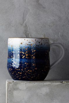 a blue and white coffee cup sitting on top of a block of concrete with gold speckles