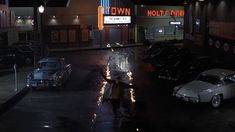 an old car parked in front of a movie theater at night with the lights on