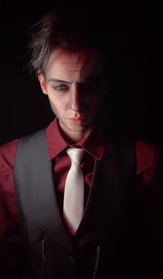 a man wearing a red shirt and black vest with a white neck tie in the dark