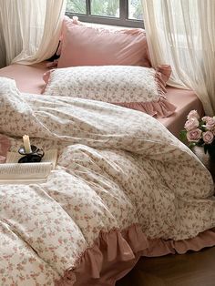 a bed with pink comforters and pillows in front of a window, next to a book