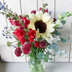 a vase filled with lots of flowers sitting on top of a wooden table next to a white wall