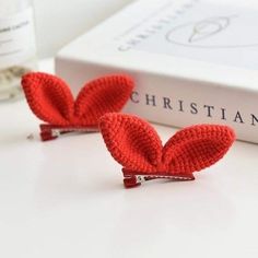 two red crocheted heart clips sitting on top of a white table next to a book