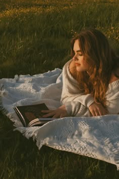 a woman laying in the grass reading a book