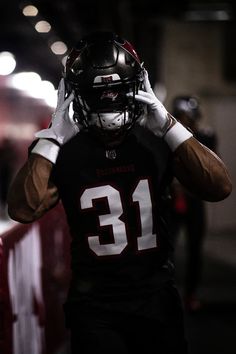 a football player is walking down the street with his helmet up to his head and hands on his ears