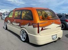 an orange and white minivan parked in a parking lot with other cars behind it