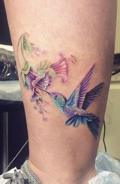 a woman's leg with a hummingbird and flowers tattoo on the side of her thigh