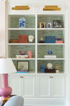 a white bookcase filled with lots of books on top of a wooden table next to a lamp