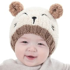 a baby wearing a knitted bear hat and smiling at the camera with one hand on his hip