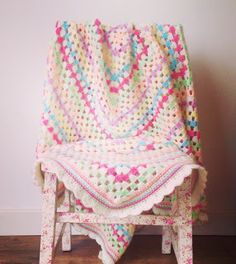 a crocheted blanket sitting on top of a wooden bench next to a wall