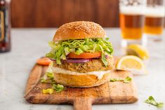 a burger with lettuce, tomato and onion on a cutting board next to a beer