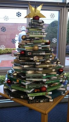 a christmas tree made out of books sitting on top of a table in front of a window