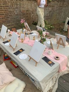 a table with several easels and paintings on it, in front of a brick wall