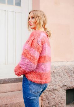 a woman wearing jeans and a pink sweater is standing on the steps with her hands in her pockets