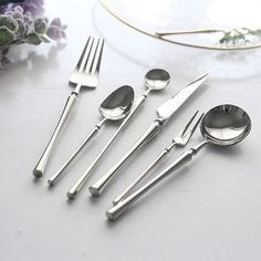 five pieces of silverware on a white table with flowers in the backgroud