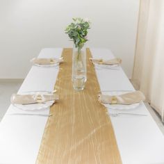 a vase with flowers is sitting on a long table set for two people to sit at