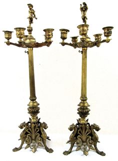 two antique brass candlesticks with figurines on the top one is standing upright