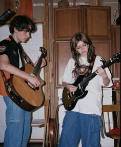 two young people playing guitars in a room