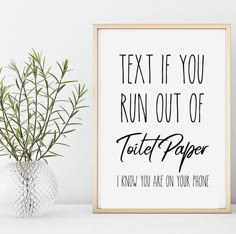 a white vase with a green plant in it next to a framed poster that says text if you run out of toilet paper i know you are on your phone