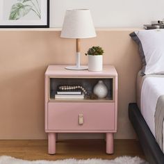 a pink nightstand next to a bed with a white lamp and pictures on the wall