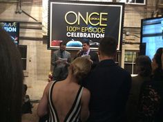 two men and a woman are standing in front of a sign that reads once on the 100th episode celebration